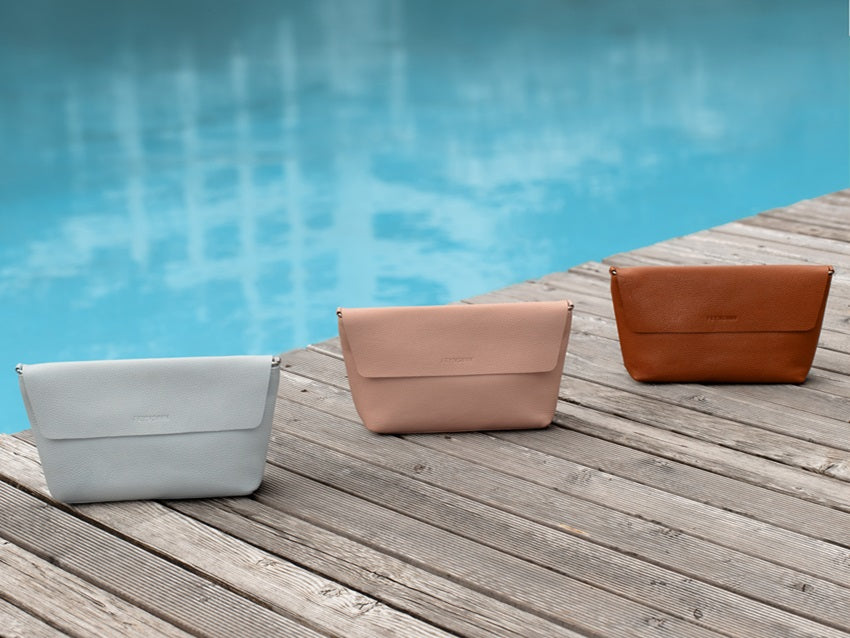 Drei Handtaschen aus Leder in unterschiedlichen Farben auf einem Steg vor einem Pool