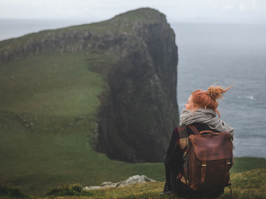 Frau mit branem Lederrucksack vor Klippen