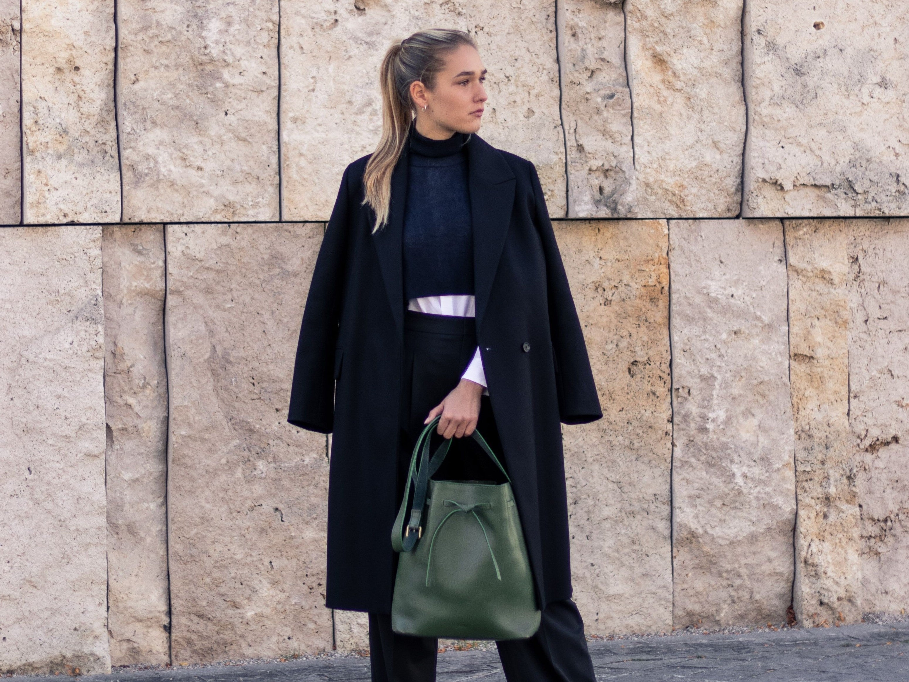 Model mit grüner Ledertasche vor Steinmauer