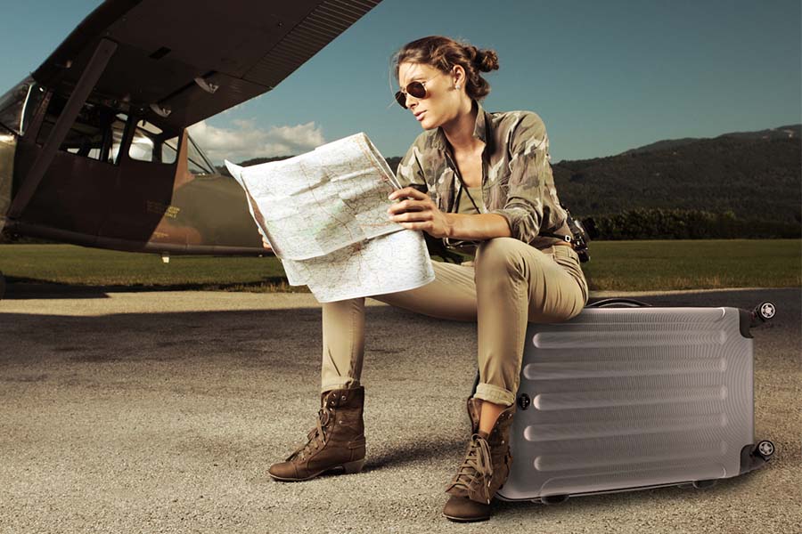 Frau sitz am Flughafen auf ihrem Koffer und liest eine Karte