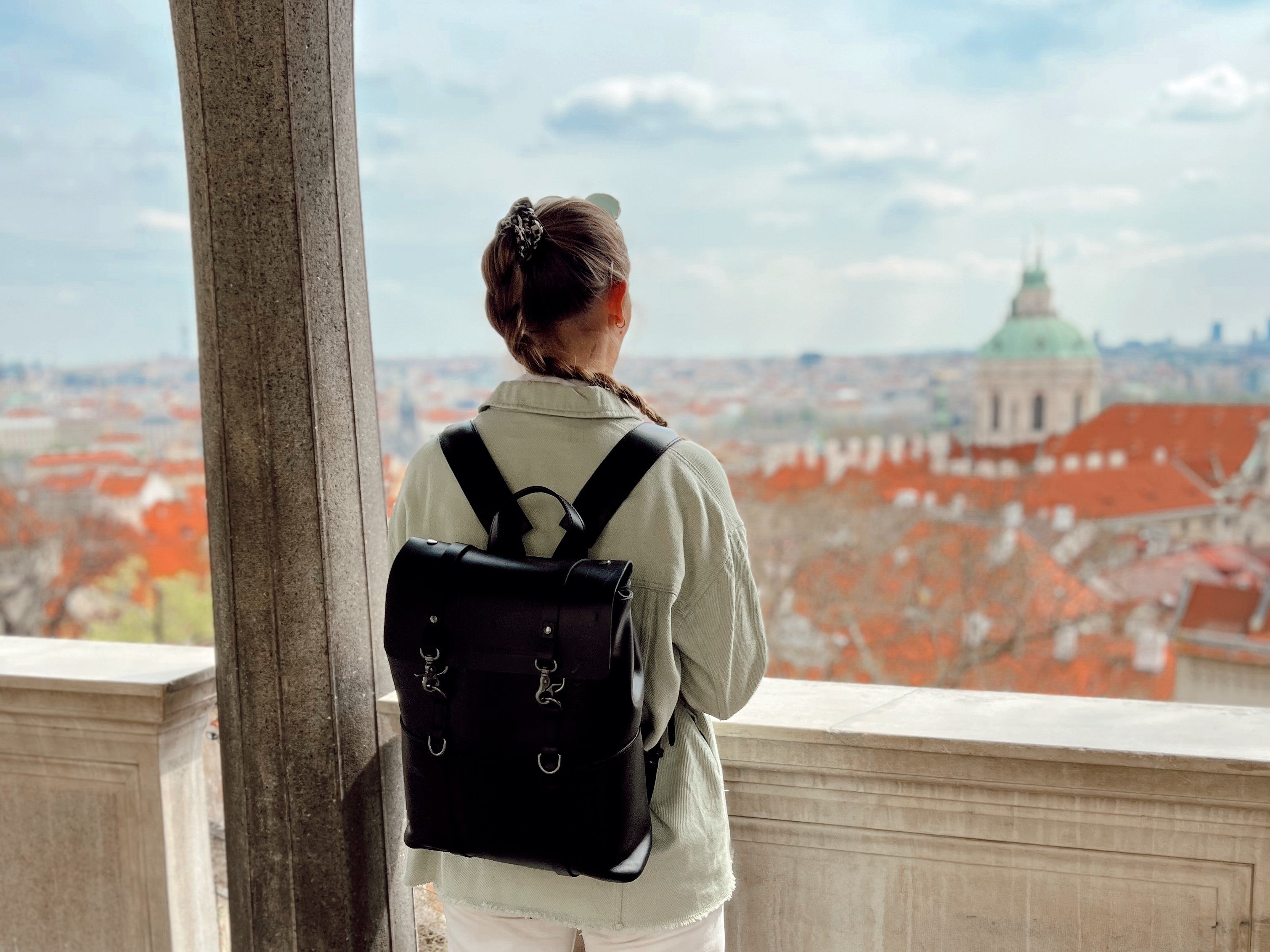 Frau mit schwarzem Lederrucksack blickt über eine Stadt