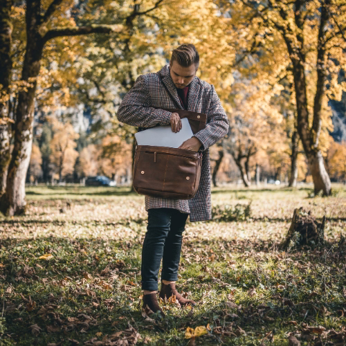 Mann in Mantel, stehend zwischen Bäumen, verstaut ein Laptop