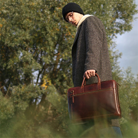 Mann mit brauner Ledertasche in der Hand, umgeben von Bäumen