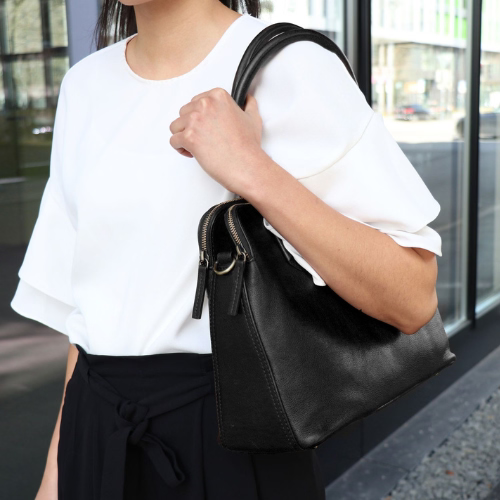 Nahaufnahme einer schwarzen Ledertasche, die von einer Frau über der Schulter getragen wird