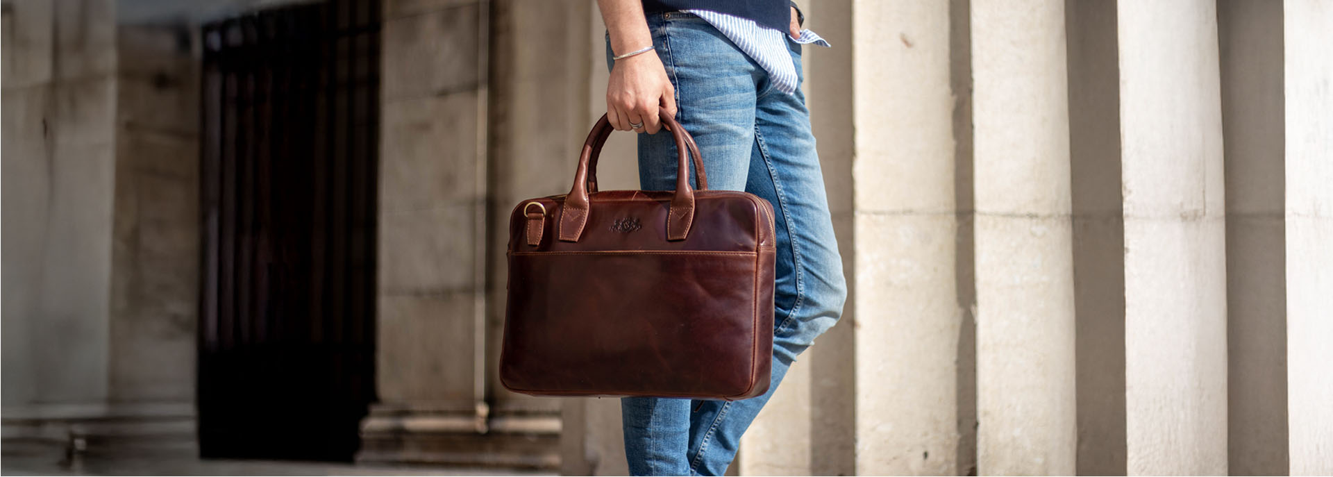 Laptoptasche aus braunen Leder in der Hand eines Mannes mit blauer Jeans