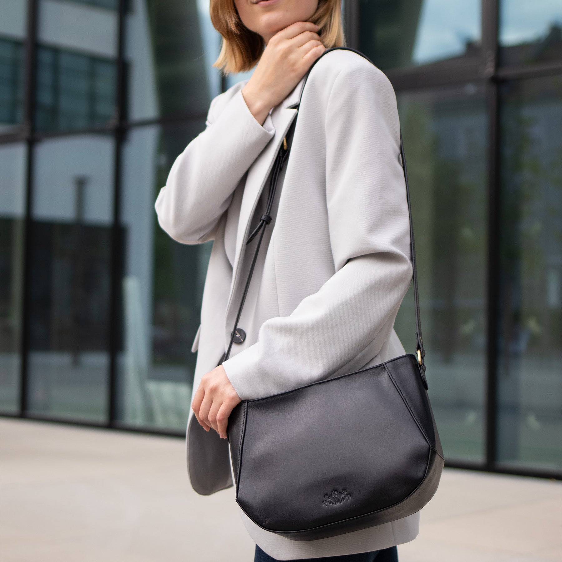 Frau mit grauer Jacke und schwarzer Ledertasche über der Schulter