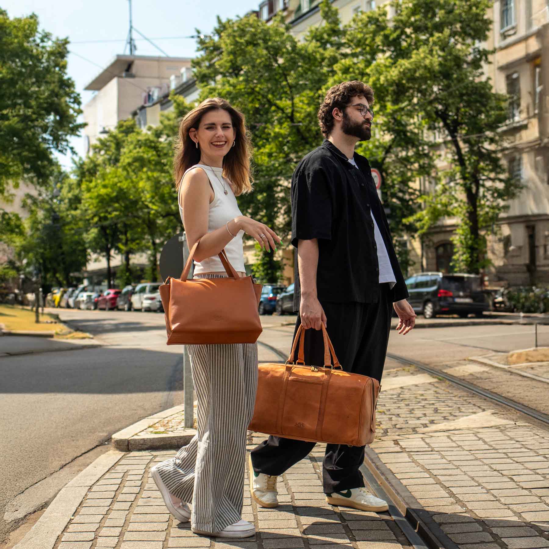 Mann und Frau mit hellbrauner Handtasche und Reisetasche aus Leder in der Stadt