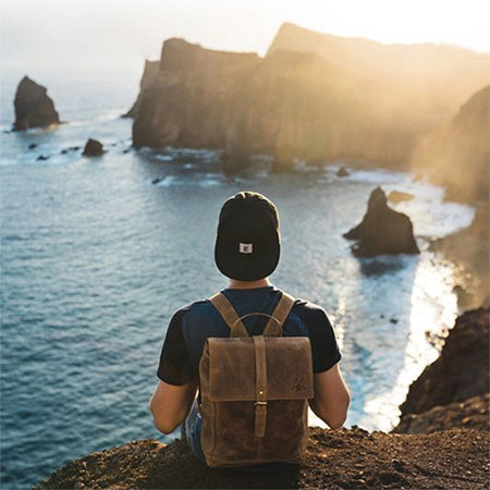 Herren Rucksack Mann sitzt und schaut aufs Meer beim Sonnenuntergang
