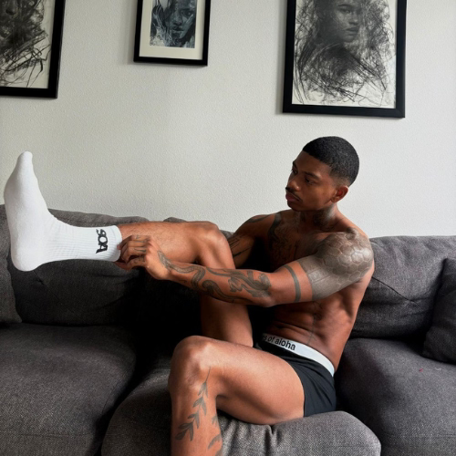 Mann zieht sich eine Socke an und traegt eine schwarze Boxershorts mit weißem Bund