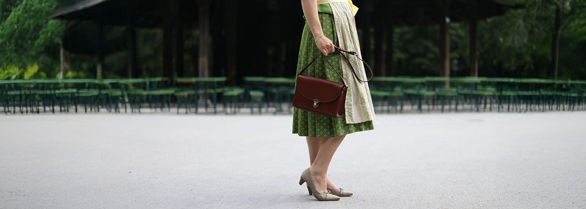 Frau in grüner Tracht mit Schultertasche aus Glattleder in braun im englischen Garten am chinesischen Turm