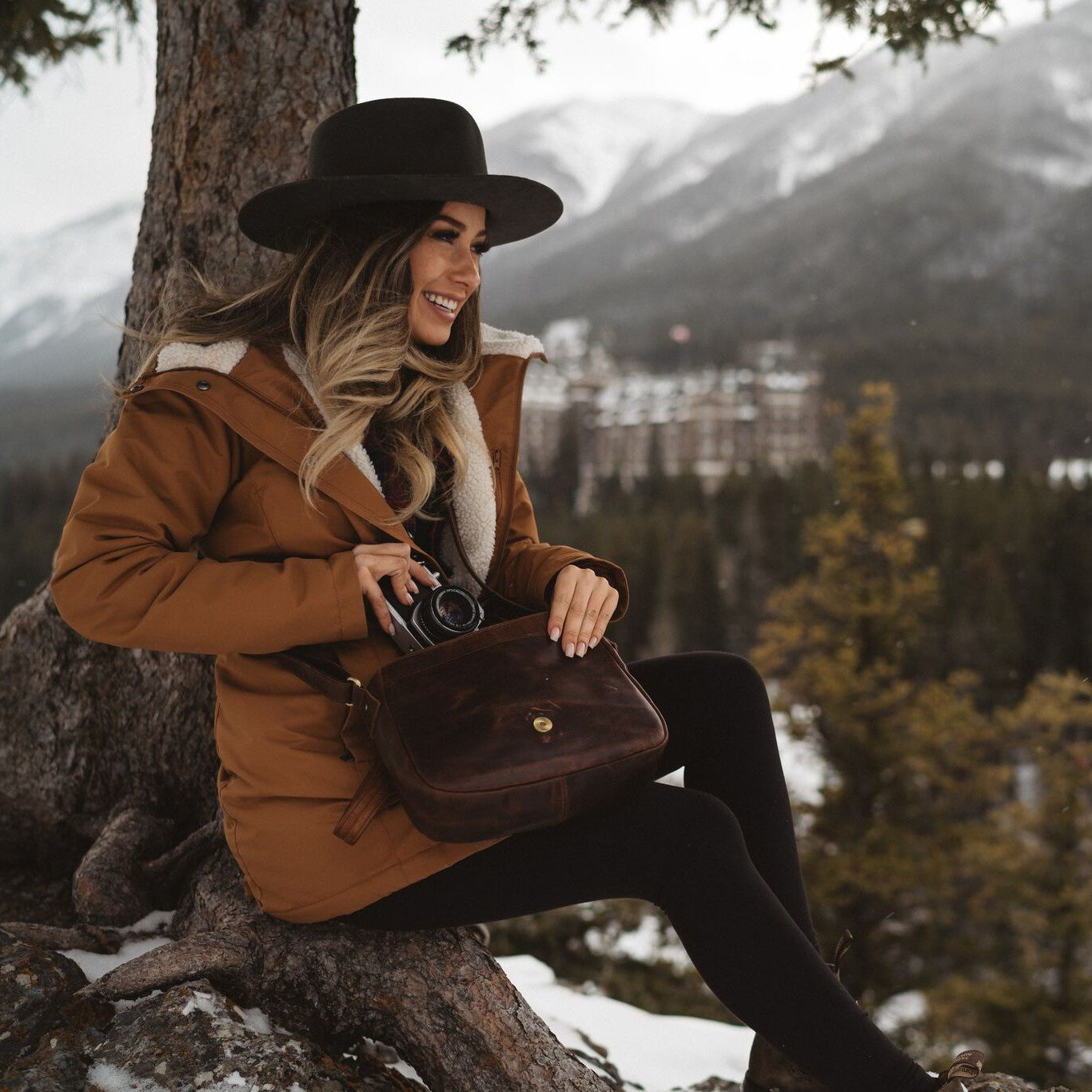 Sid and Vain Umhängetasche Leder YALE dunkelbraun Frau sitzt draußen in den Bergen und traegt eine Winterjacke und einen Hut