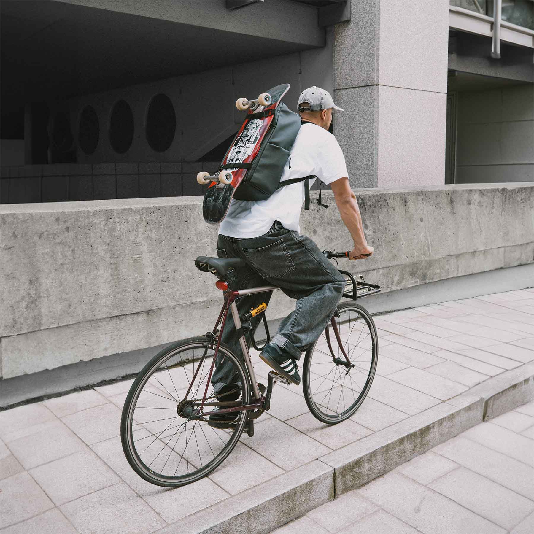 Rucksack AHI auf Rücken von Fahrradfahrer in der Stadt. Rucksack hält ein Skateboard