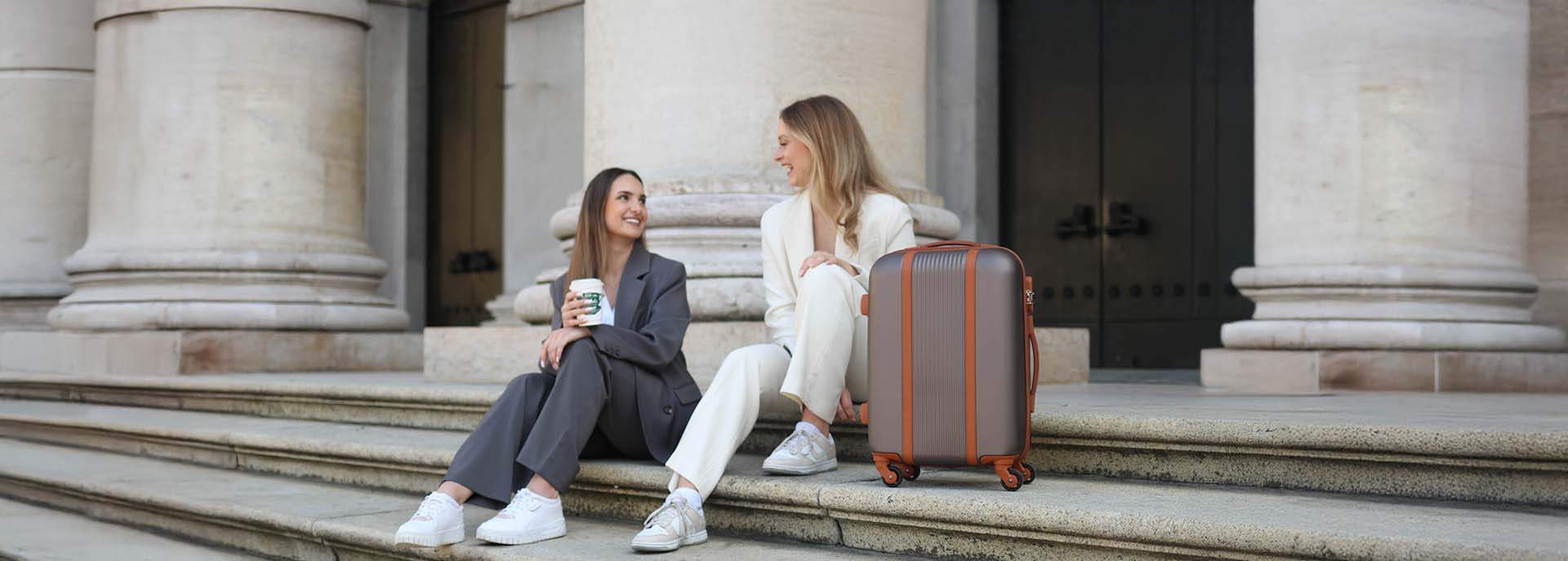 Koffer in braun und zwei Frauen auf einer Treppe mit Säulen in Italien
