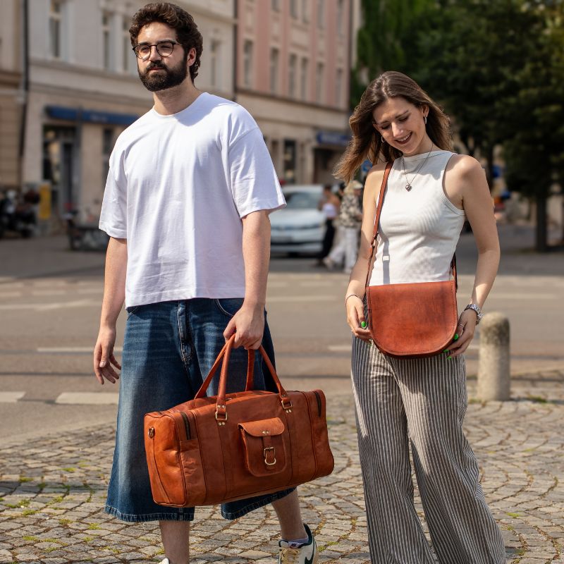 Mann traegt eine Reisetasche aus Leder in der Hand und die Frau traegt eine Umhaengetasche Leder und sie gehen in der Stadt
