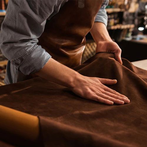 Material Leder Mann ist in seiner Werkstatt und breitet das Leder vor sich aus braun