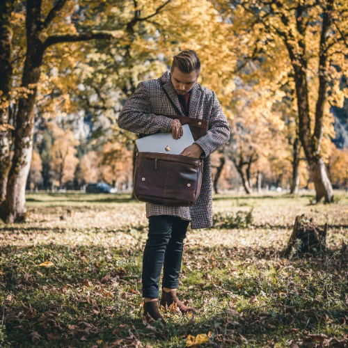 Mann in einem Park, hebt einen Laptop aus einer braunen Ledertasche