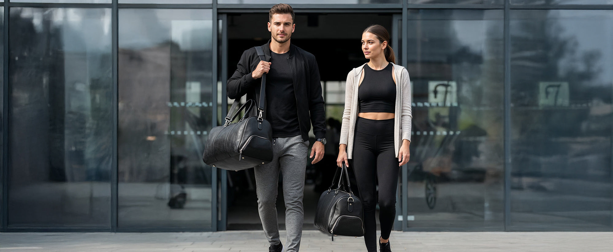 Eine attraktive Frau in Sportkleidung und in sportlicher Mann verlassen das Gym mit ihren Sporttaschen aus Leder