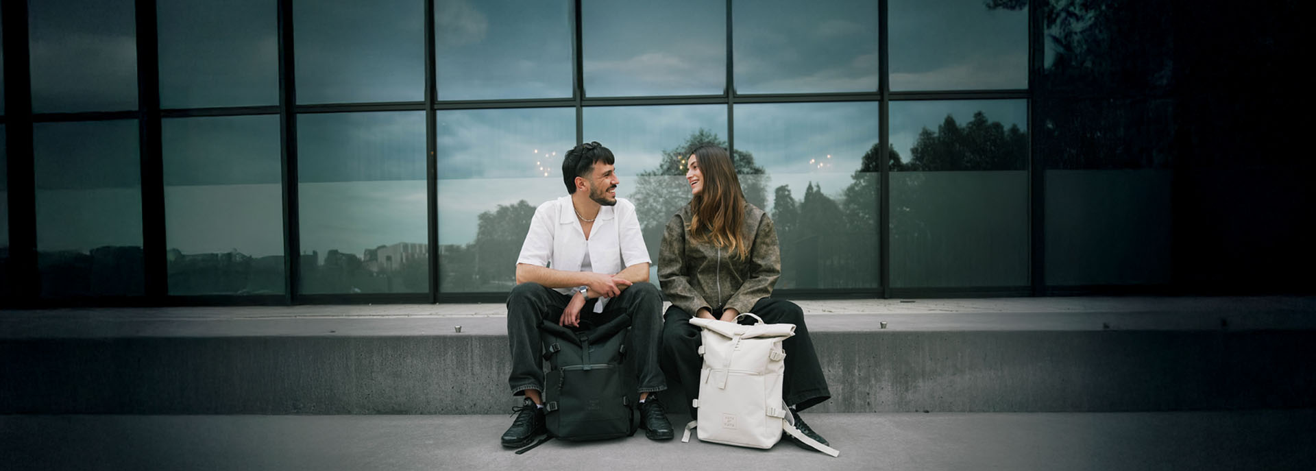 Universität mit Junge und Mädchen. Beide haben einen Roll-Top Rucksack in beige und schwarz