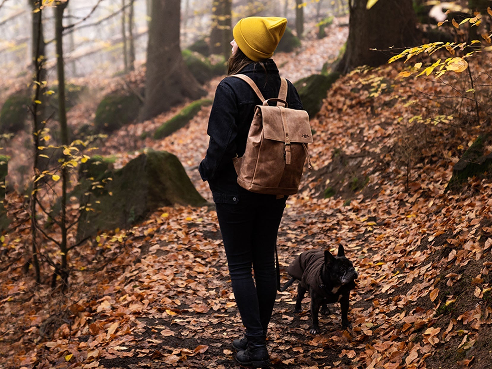 Frau mit Hund und Lederrucksack in einem Wald