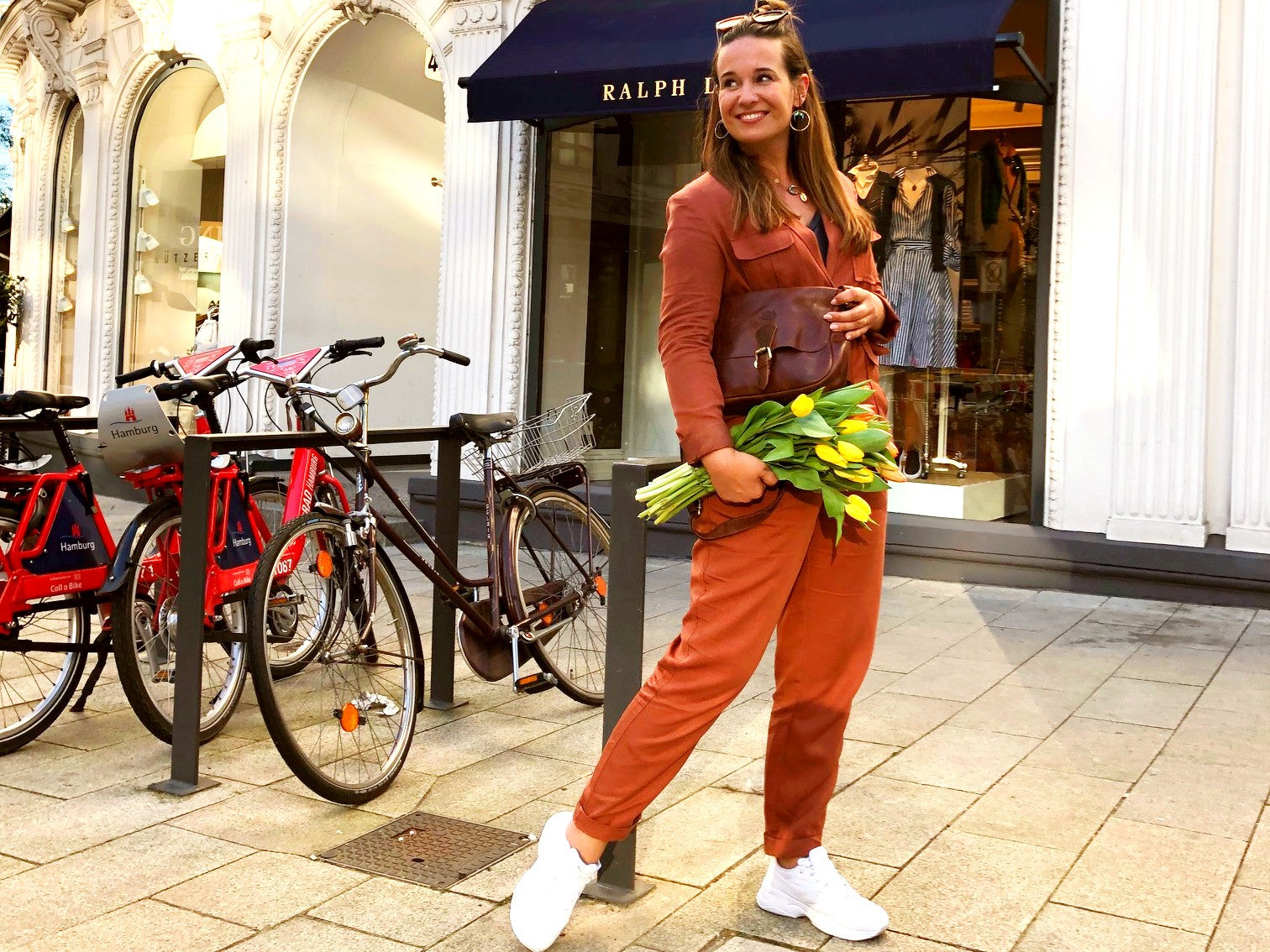 Frau mit Blumen und Ledertasche vor einem Laden