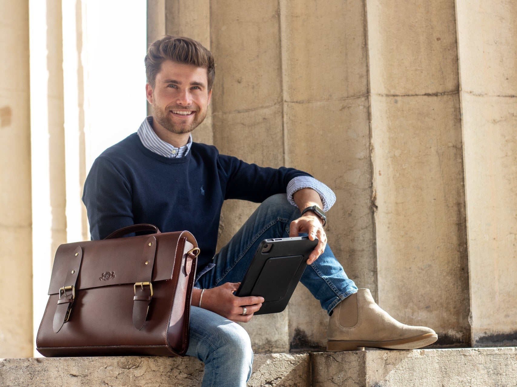 Mann mit Tablet und brauner Aktentasche sitzend vor einer Säule