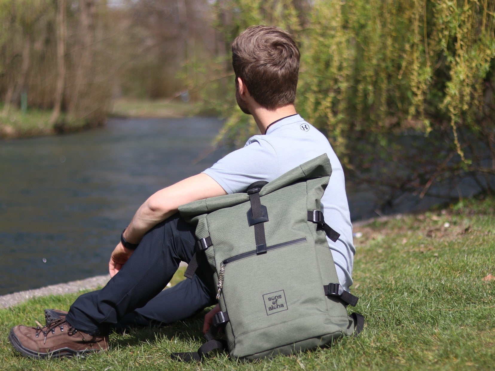 Mann mit Rolltoprucksack KANE sitzend auf einer Wiese