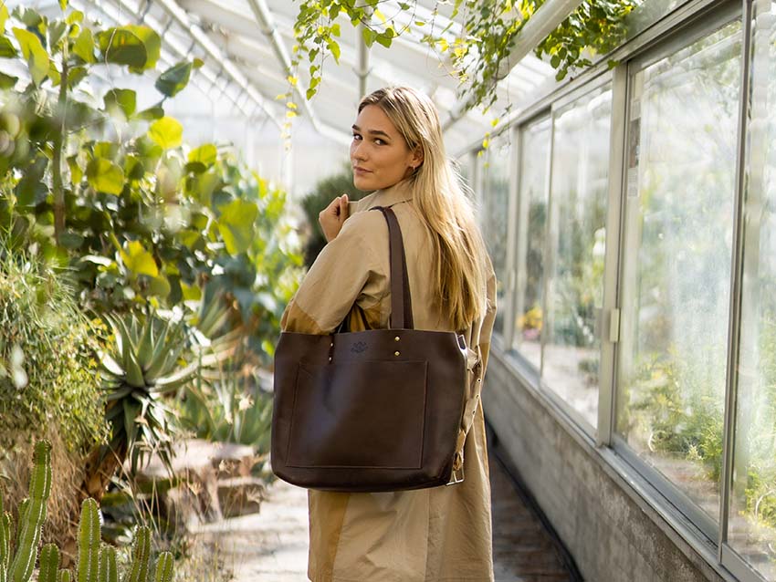 Frau mit großer, brauner Ledertasche in einem Gewächshaus
