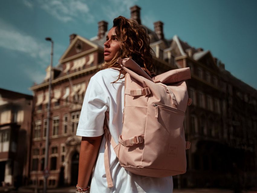 Eine Frau mit einem pinken Rolltop Rucksack vor einem großen Gebäude