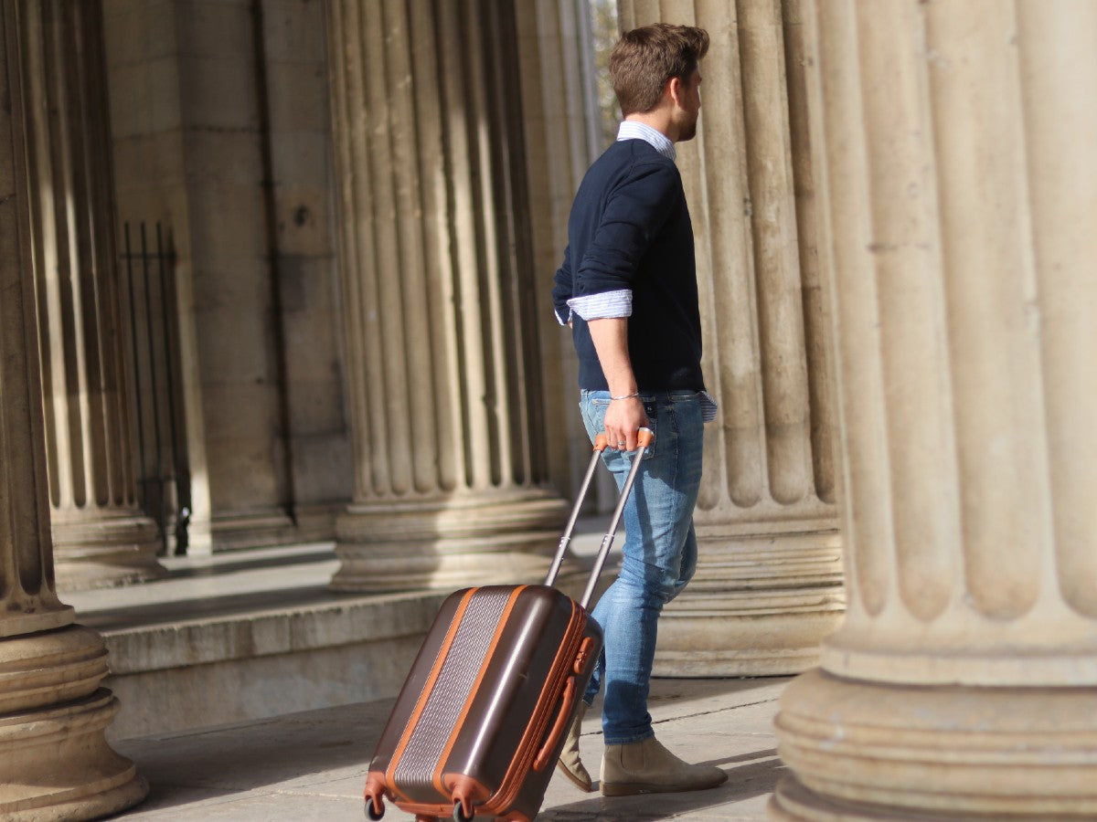 Mann mit braunem Reisekoffer, stehend zwischen Säulen