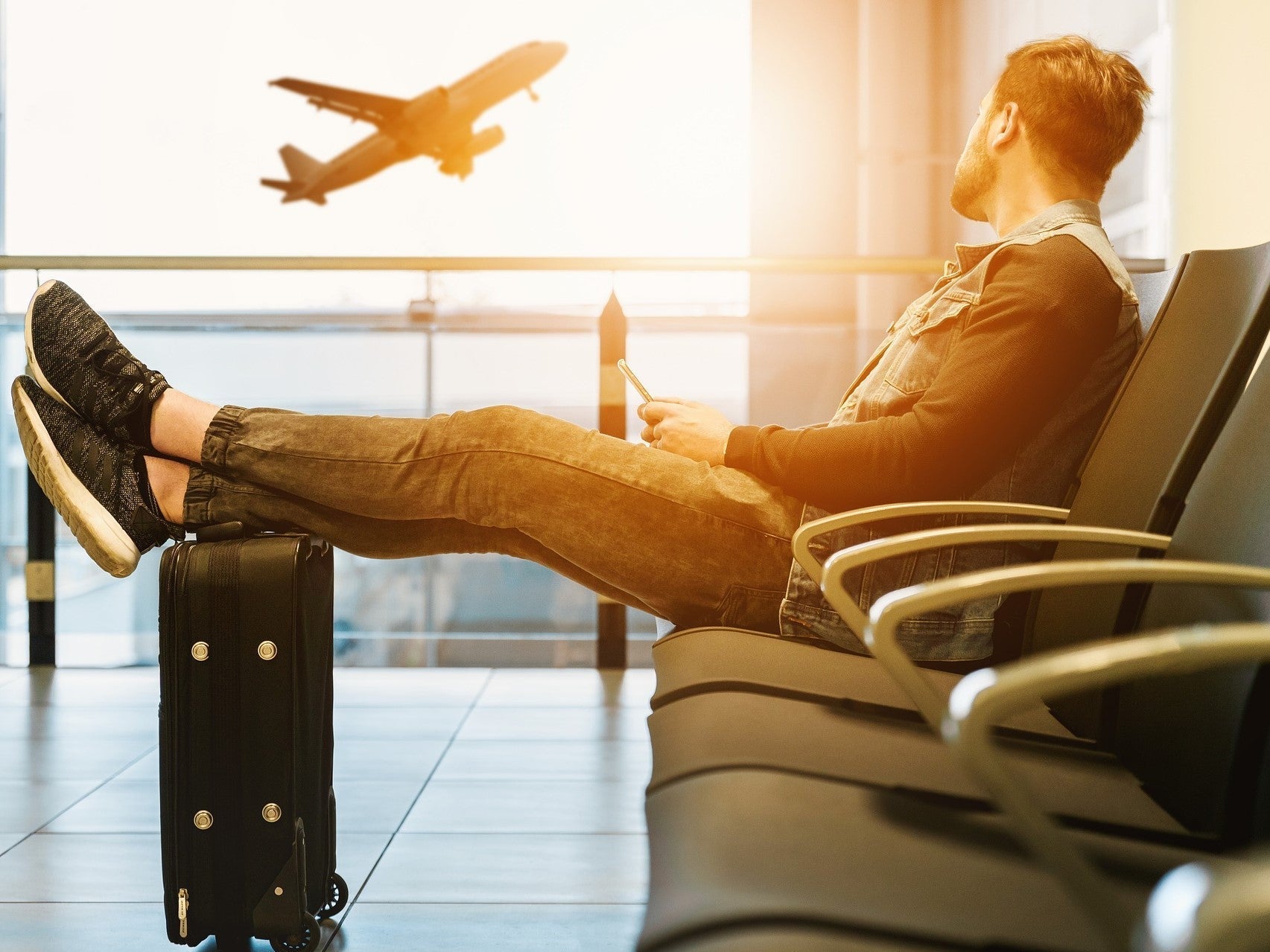 Mann sitzend in einem Flughafen mit Koffer und Flugzeug im Hintergrund