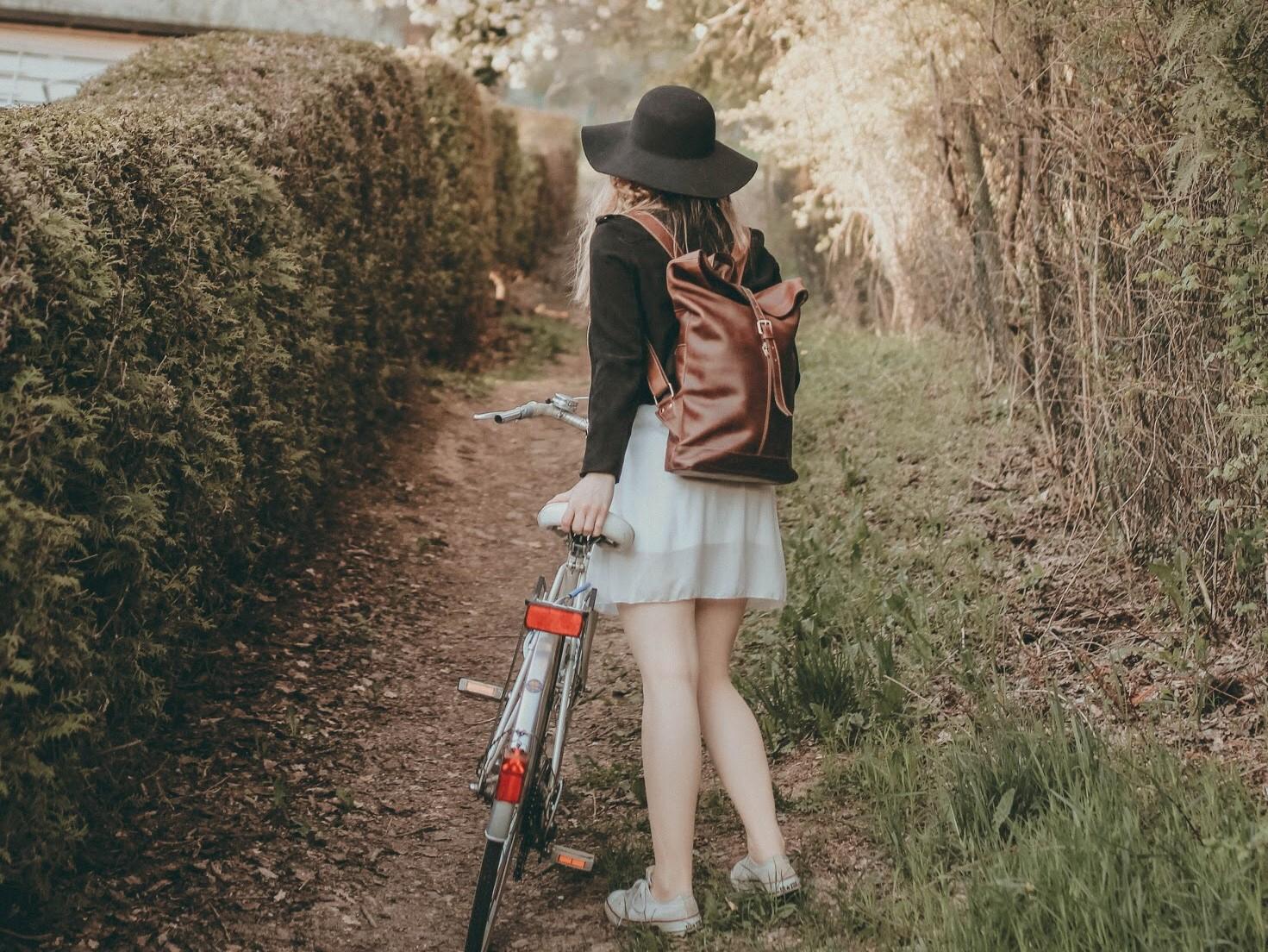 Frau mit Fahrrad und braunem Lederrucksack auf einem Feldweg