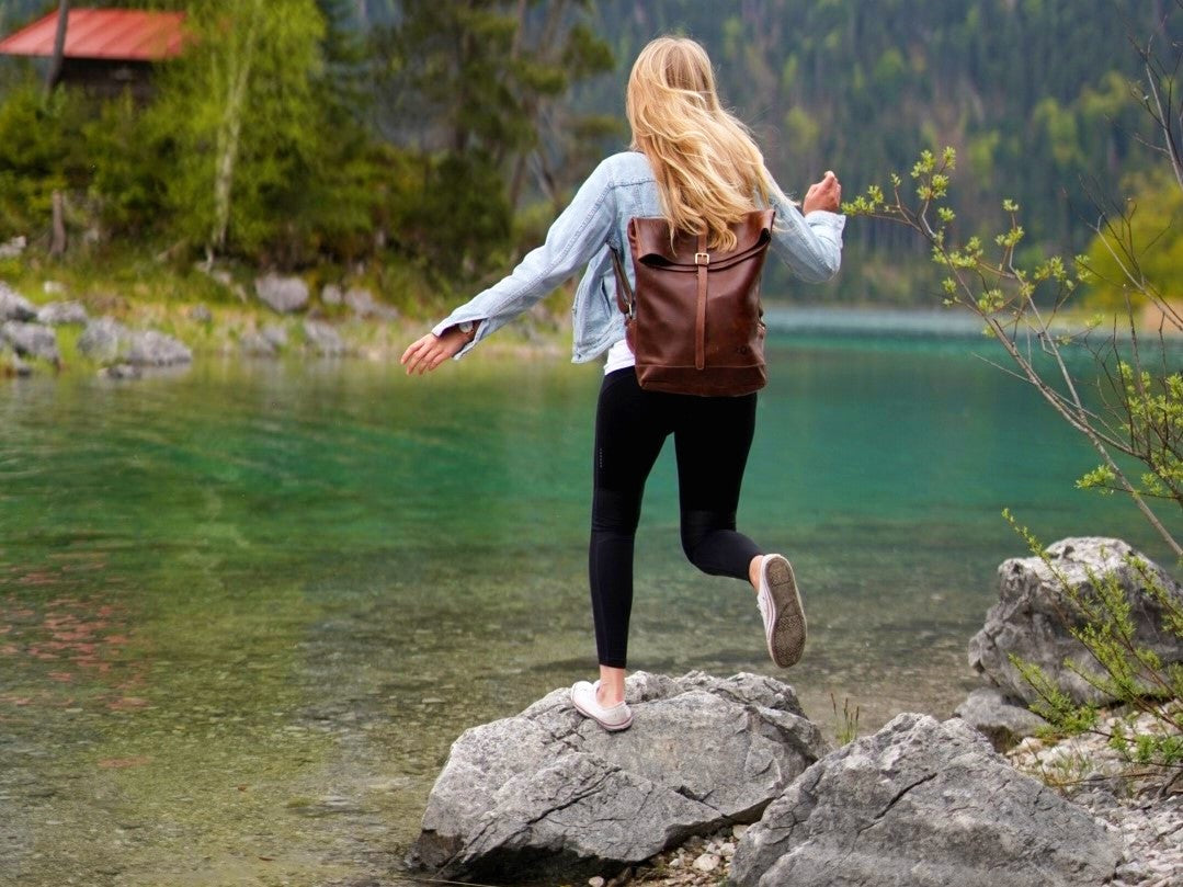 Frau mit Lederrucksack auf einem Stein an einem Flussufer