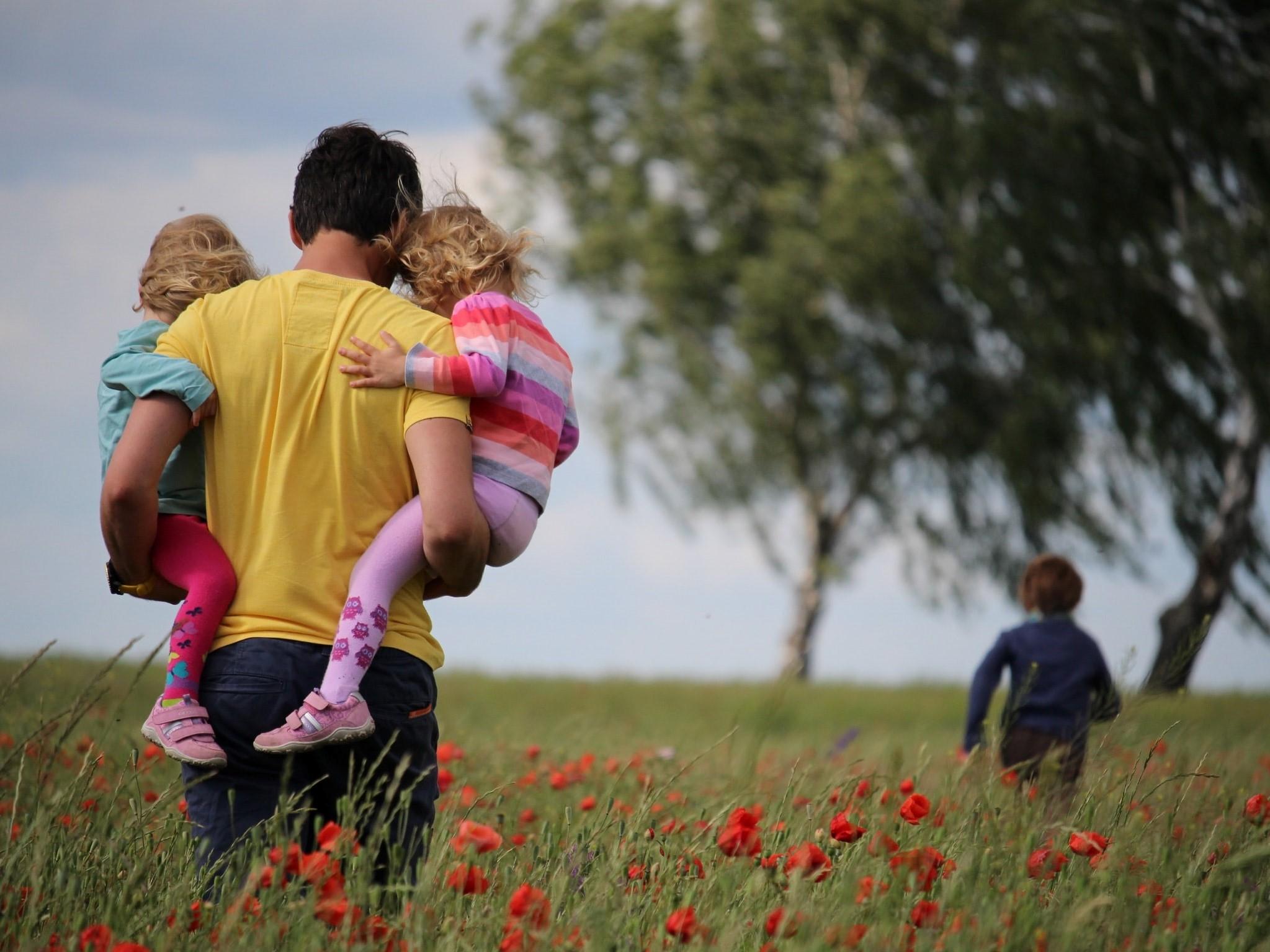 Mann mit zwei Kindern auf den Armen und einem dritten Kind im Hintergrund
