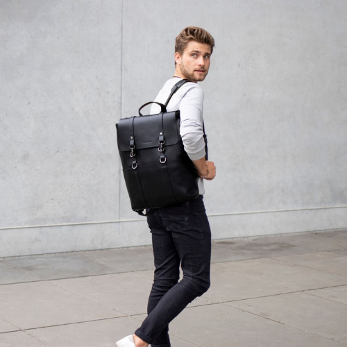 Rucksack Herren in schwarz aus Leder Mann traegt einen grauen Pulli und eine schwarze Hose
