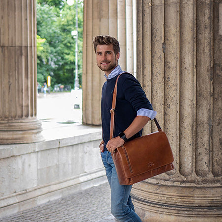 Mann mit brauner Laptoptasche aus Leder über der Schulter vor Säulen