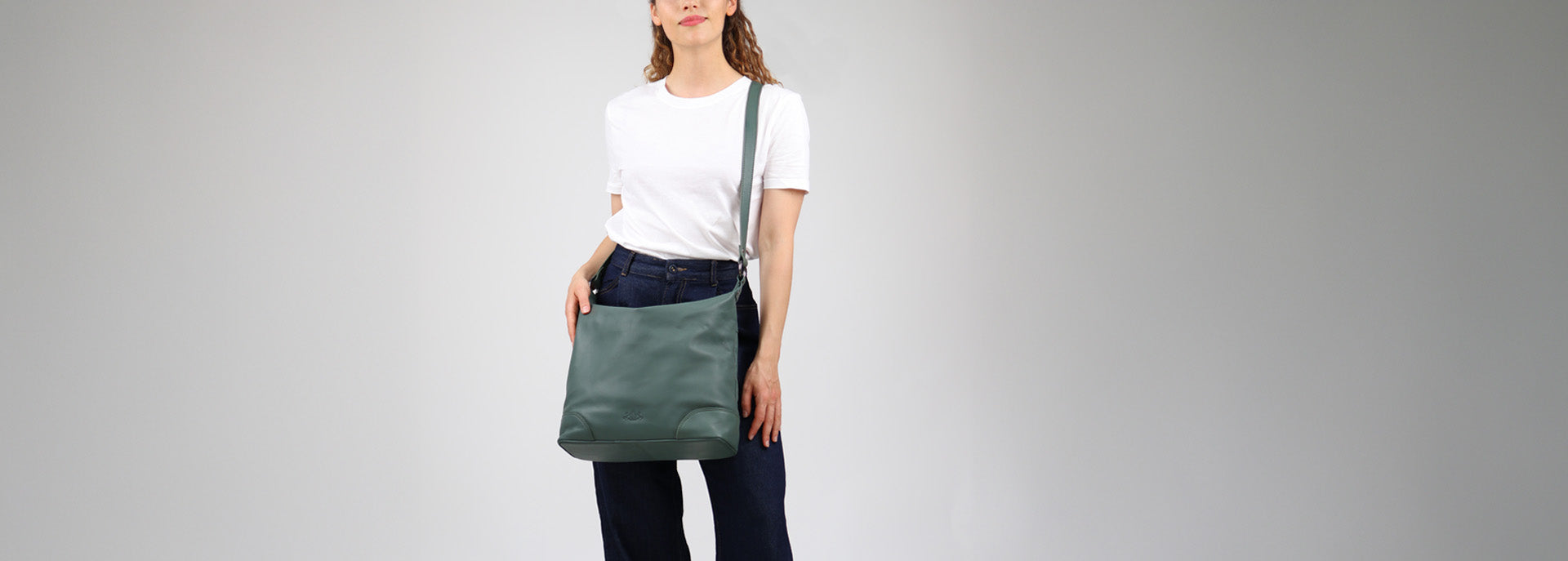 Studiobild Model mit weißen Shirt und dunkler Jeans trägt grünliche Hobo Bag aus Leder.