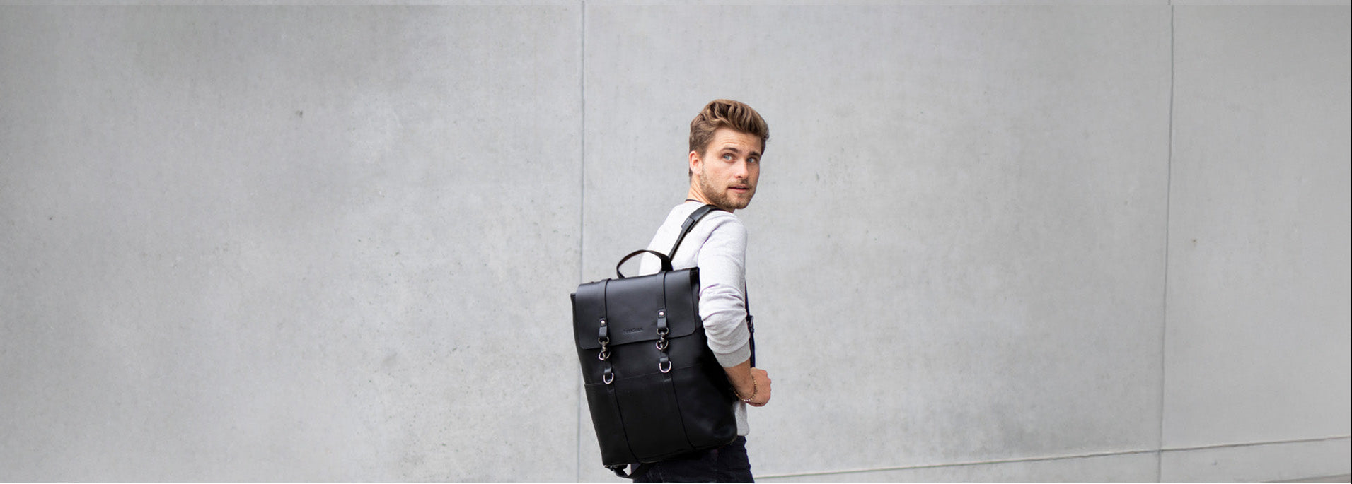 Laptoprucksack in schwarz an Mann vor modernem Gebäude