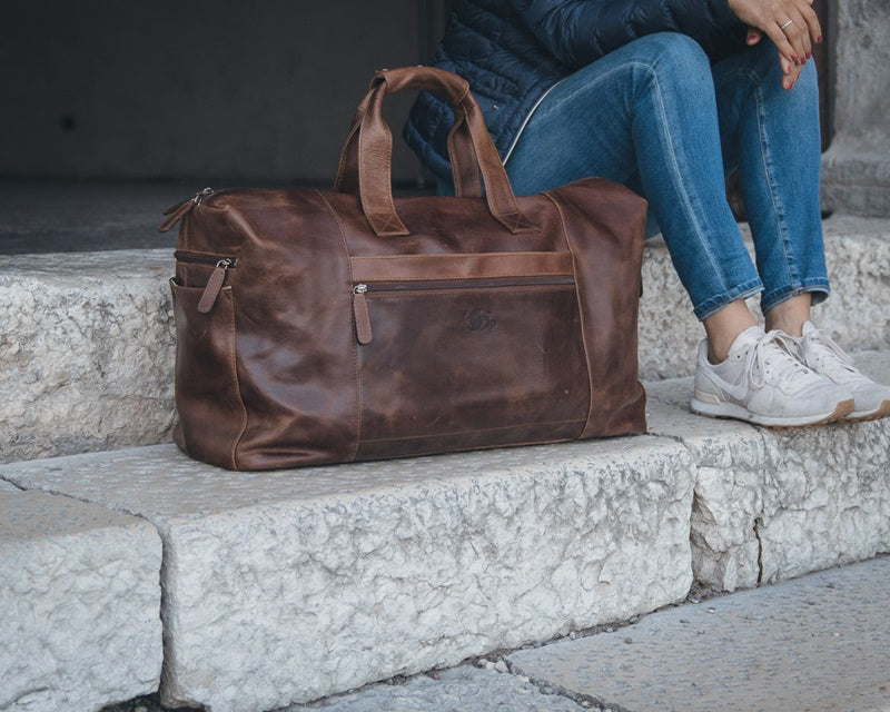 Reisetasche Damen Leder in  braun Frau traegt weiße Sneaker und eine blaue Jeans und eine Steppjacke