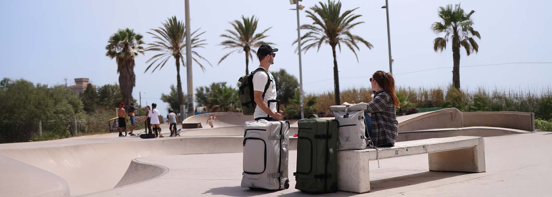 Reisetasche mit Rollen in hellem grau und oliv mit einem Mann und einer Frau an einem Skateplatz in Barcelona