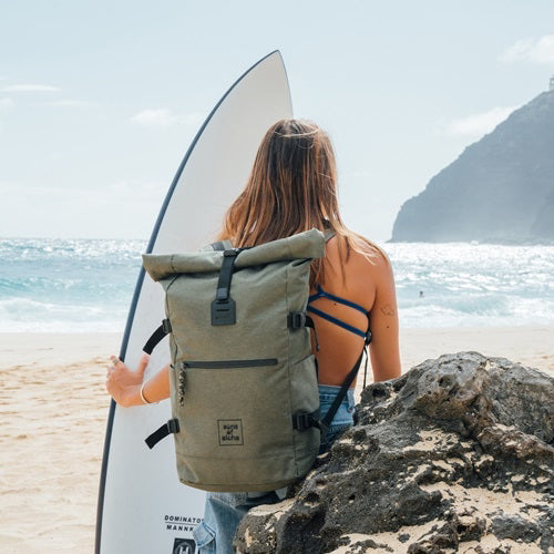 Reiserucksack Damen recyceltes Materil in olive gruen Frau steht am Strand und haelt ein Surfbrett in der Hand