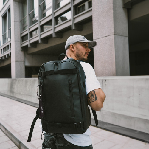 Rucksack nachhaltig AHI in schwarz. Mann traegt eine Cap und traegt ein weißes T-Shirt