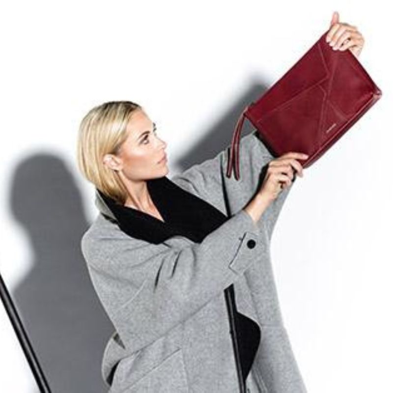 Clutch Frau traegt einen grauen Mantel und hält eine rote Clutch