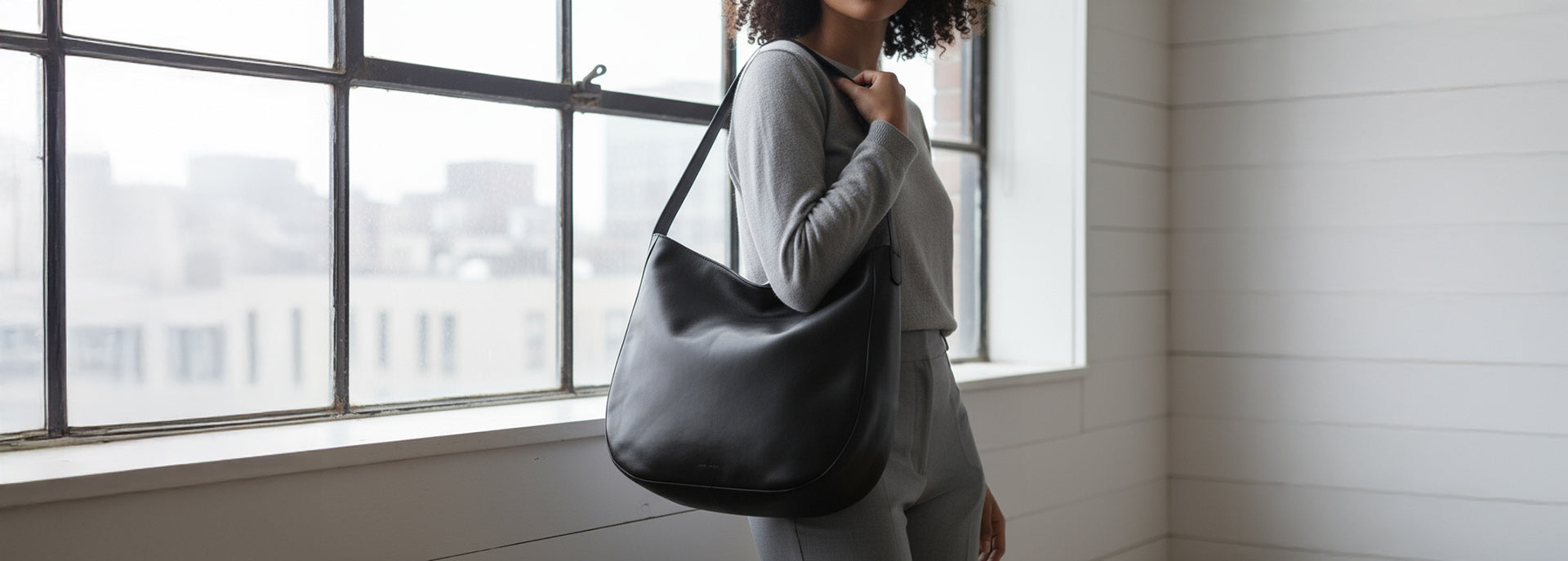 Studiobild Model mit grauen modernen kleidung trägt eine schöne schwarze Hobo Bag aus weichem Leder.
