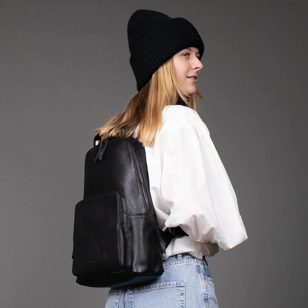 Wir sehen eine urbane Frau mit einem schwarzen Laptoprucksack aus weichem schwarzen Leder