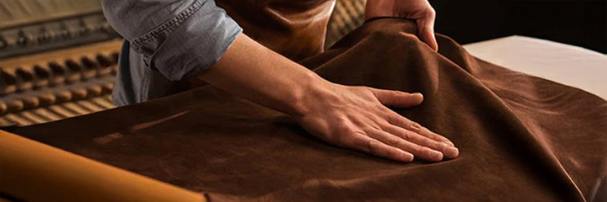 Material Leder Mann ist in seiner Werkstatt und breitet das Leder vor sich aus braun