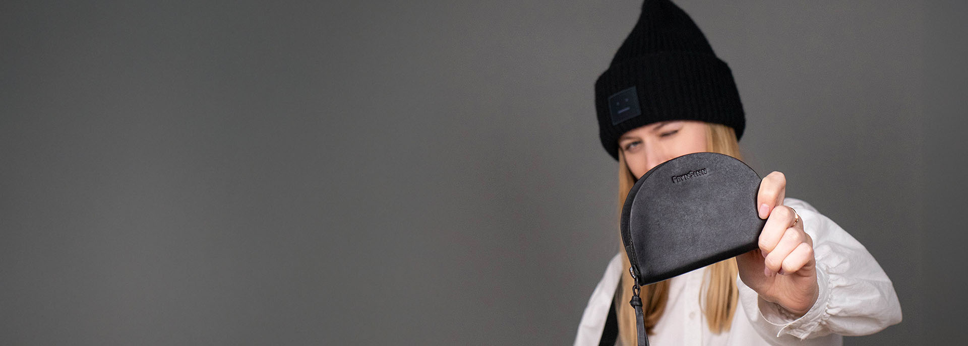 Frau hält schwarzen Leder-Geldbeutel in die Kamera. Sie trägt eine weiße Bluse und eine schwarze Beanie