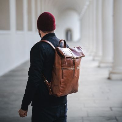 Sid and Vain Herren Rucksack Leder in braun zum einrollen Mann traegt rote Mütze und dunkelblaue Jacke