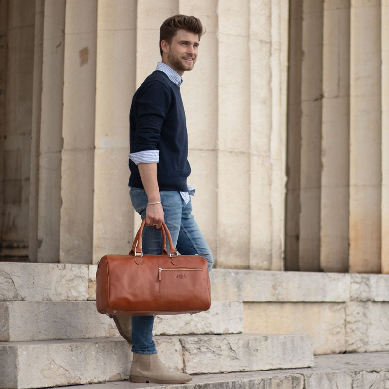 Weekender Herren Leder Mann taegt einen dunkelblauen Pulli und eine helle Jeans